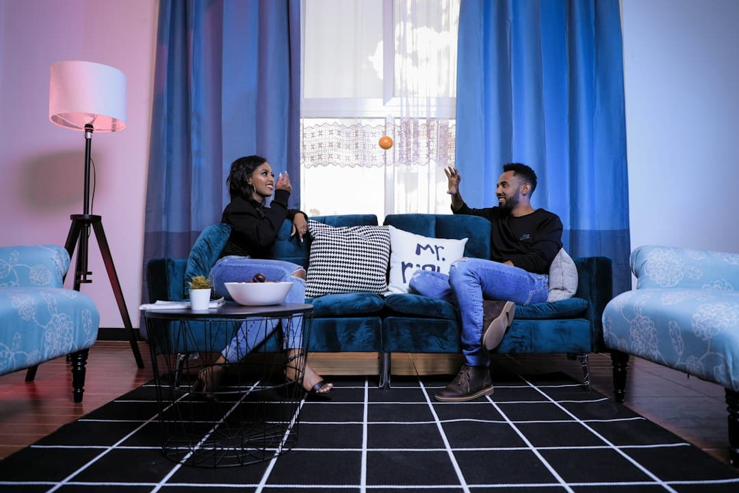 Two people talking on a blue sofa in a bright living room, deciding on the best IPTV service, such as Digitaline IPTV