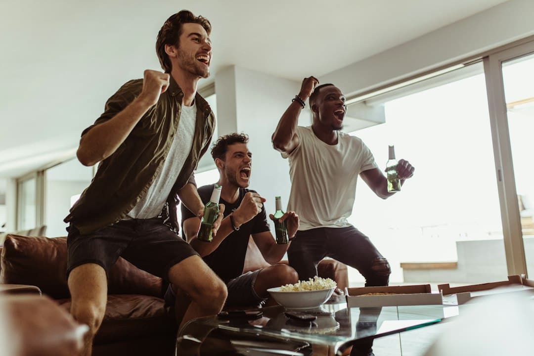 Friends cheering on the sofa with popcorn on game day, watching live sports with Digitaline IPTV
